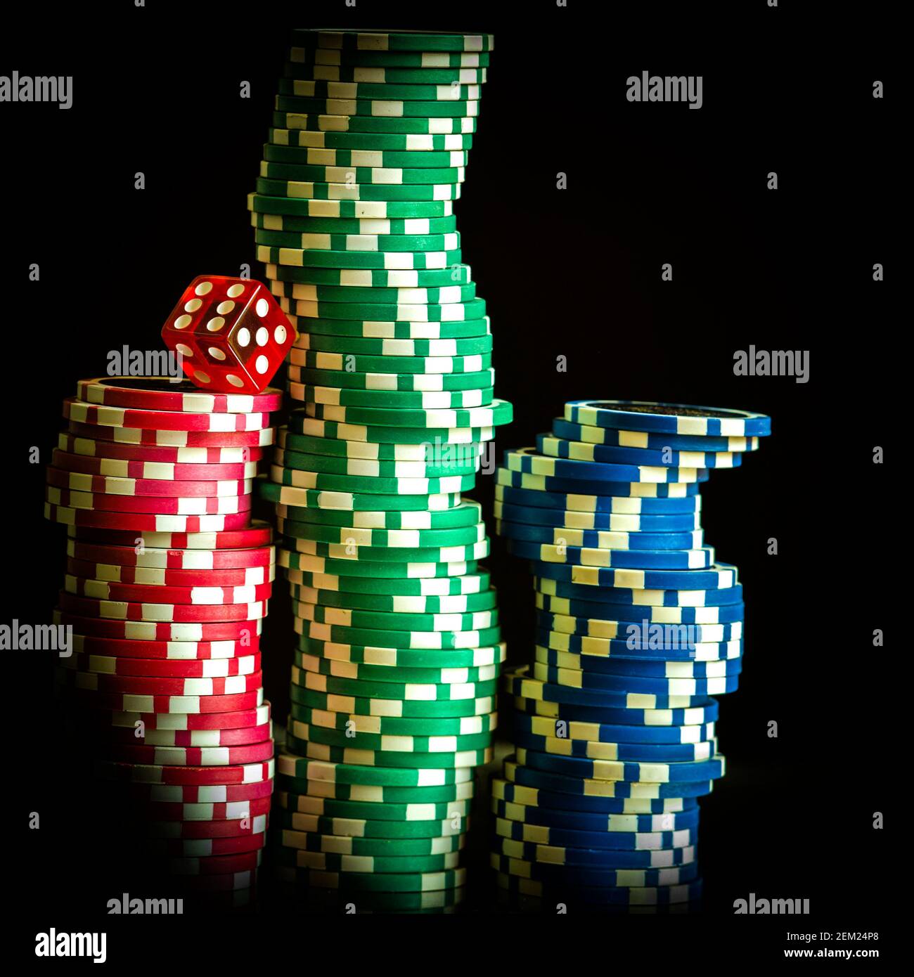 Pile di chip colorate da poker con un dado rosso su sfondo scuro, perfette per gli appassionati di giochi e per i giochi d'azzardo Foto Stock