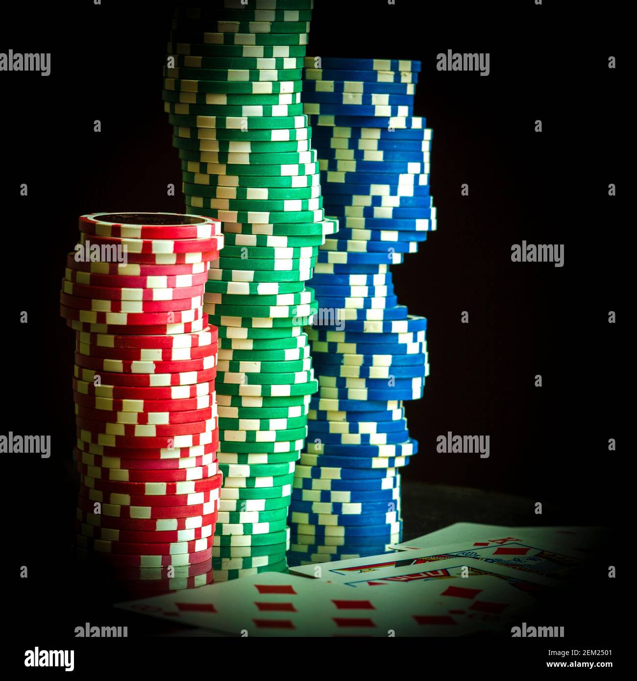 Pile di colorate patatine da poker con carte da gioco su un tavolo in una sala da gioco durante una partita di poker in tarda serata Foto Stock