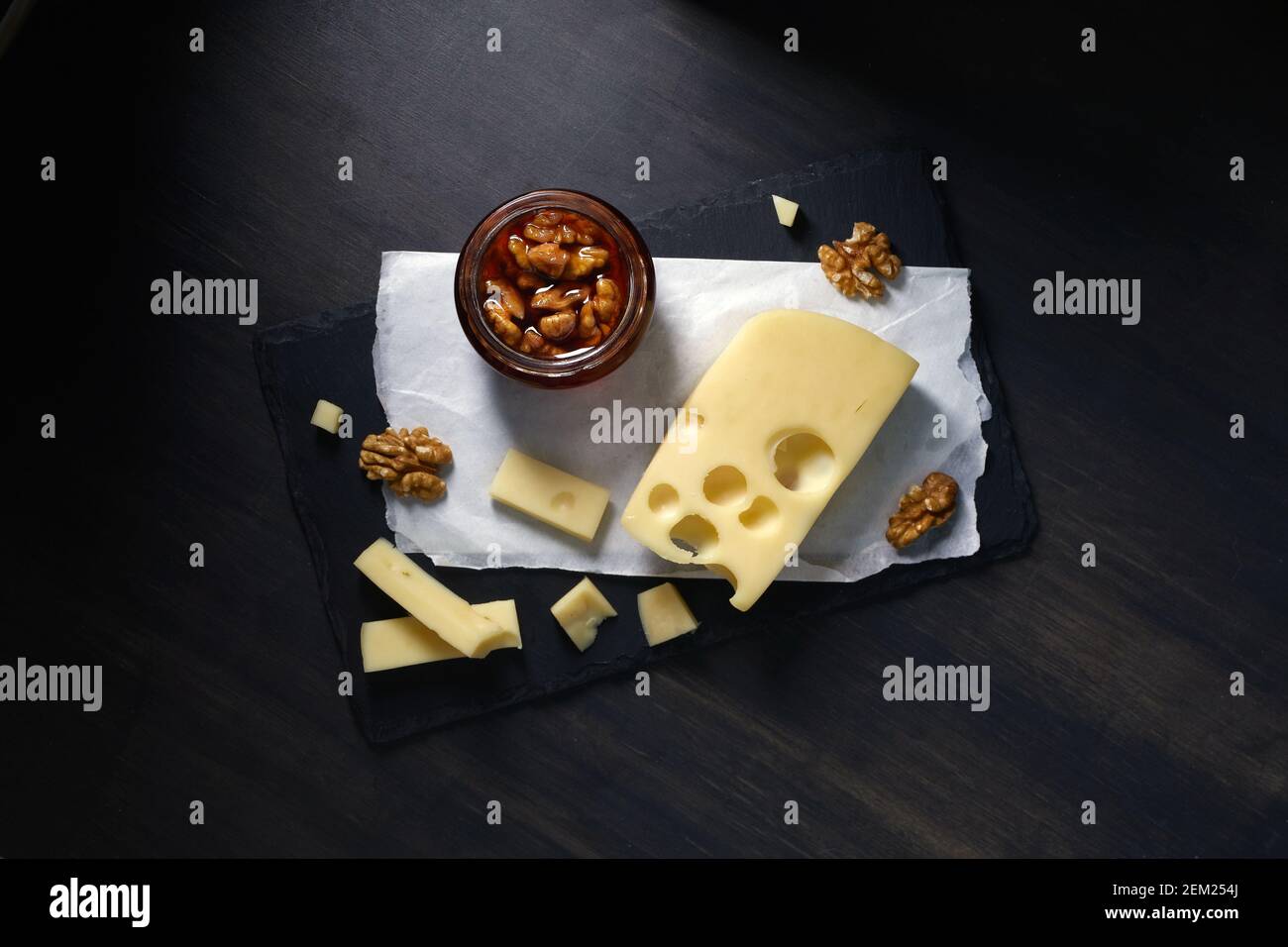 il formaggio semirigido di maasdam tagliato a fette giace su un piatto di pietra con miele e noce su sfondo scuro Foto Stock