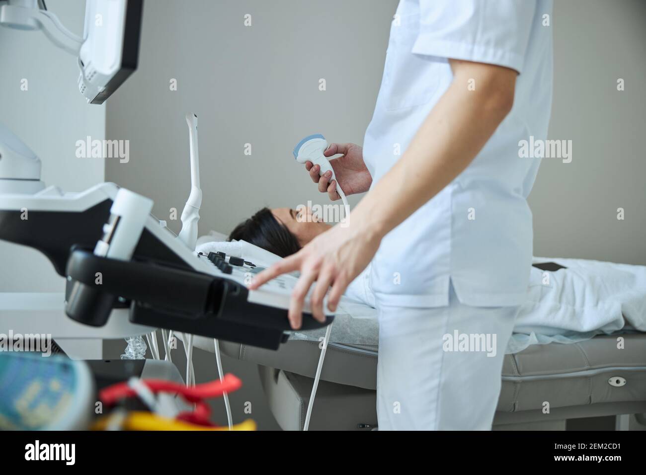Medico con un trasduttore in piedi davanti a una console di un apparecchio di ecografia Foto Stock