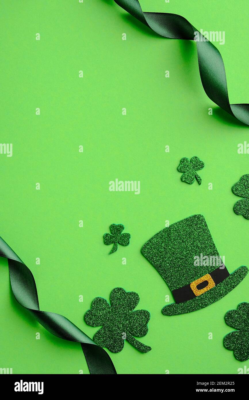 St Patricks Day con banner verticale. Piatto, vista dall'alto cappello leprechaun, foglie shamrock e nastro su sfondo verde. Giorno di San Patrizio minimo c Foto Stock
