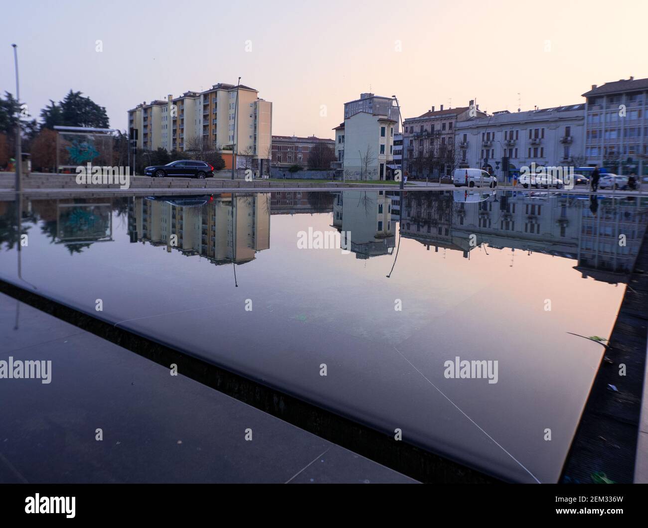 Città riflessa in uno specchio a bordo piscina al tramonto.Legnano, città metropolitana di Milano, Italia. Foto Stock