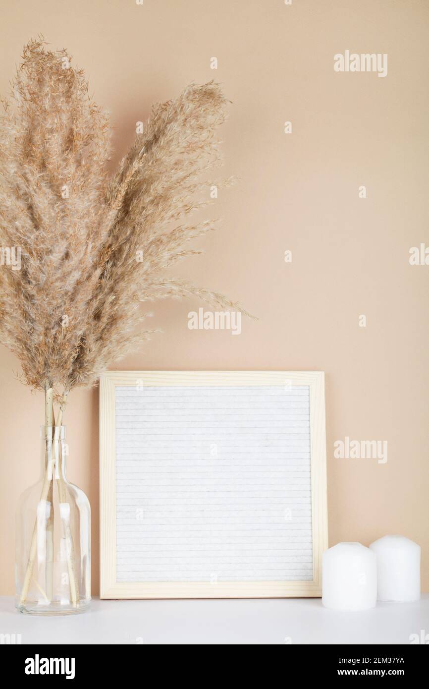 Erba secca di pampas in vasi, candele e carta da lettera su sfondo beige, interni, design domestico. Concetto di arte. Spazio di copia Foto Stock