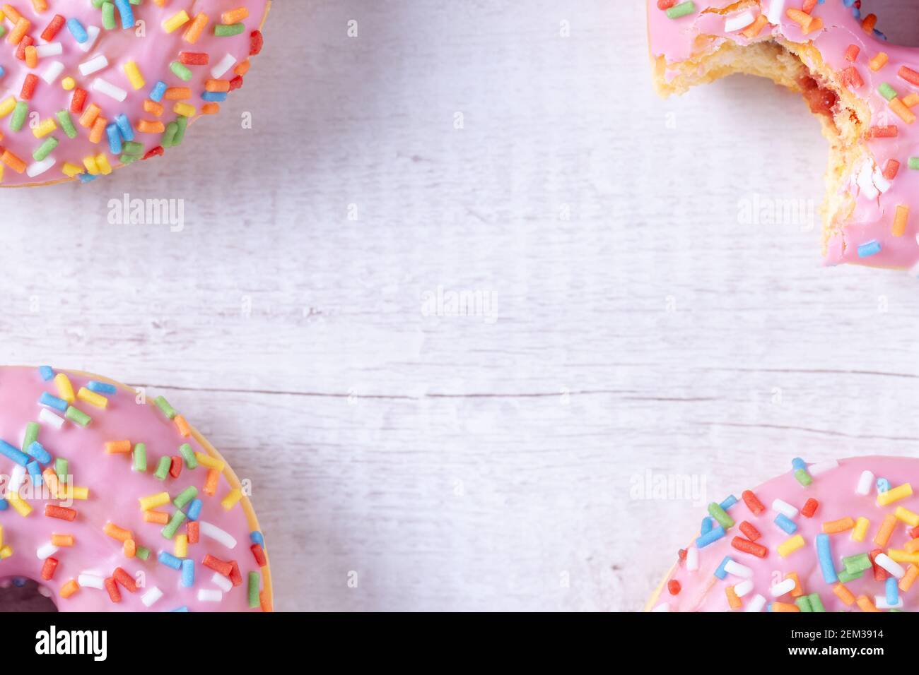 Deliziose ciambelle con glassa rosa, ripieno di gelatina di fragole e coloratissime spruzzette su sfondo di legno con spazio per la copia. Dolce pasticceria americana. Foto Stock