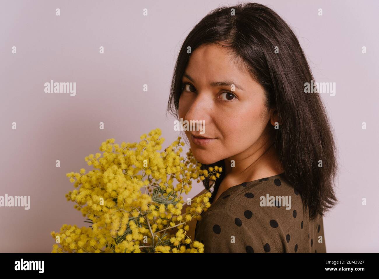 festa del giorno della donna. guardaroba di giovane donna che tiene mimosa fiori mumosa giallo bouquet su sfondo bianco sorridendo con vestiti casual guardando camer Foto Stock