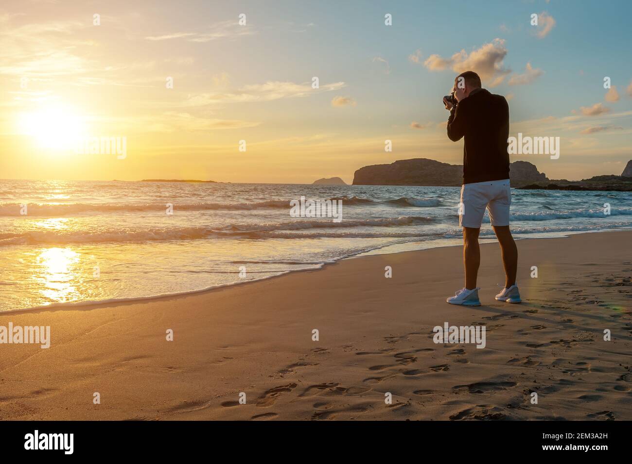 Uomo che scatta foto su una spiaggia tropicale durante il tramonto. Concetto di vacanza e viaggio. Foto Stock