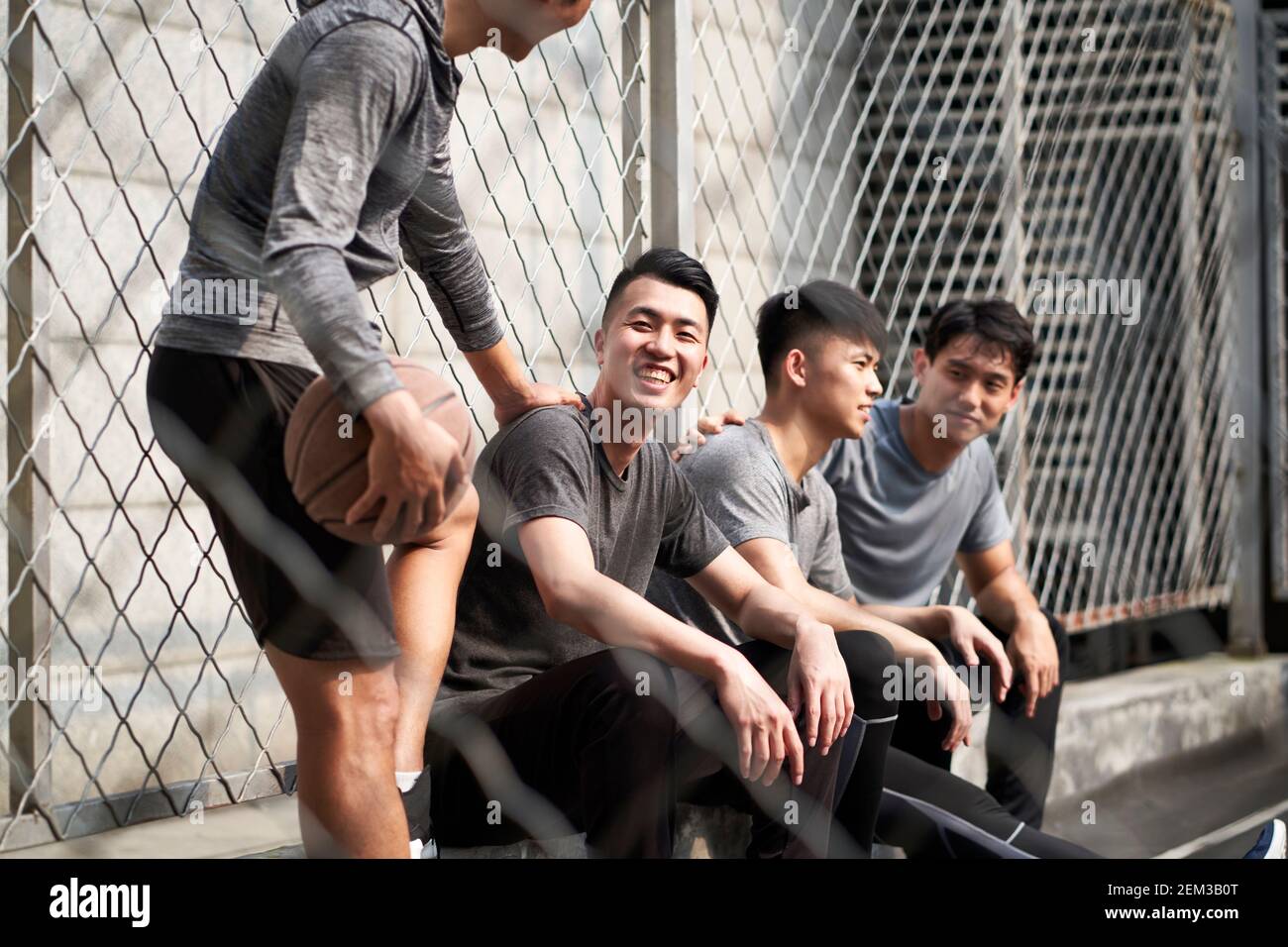 gruppo di quattro giovani adulti asiatici che riposano mentre chiacchierano sul campo da pallacanestro all'aperto Foto Stock