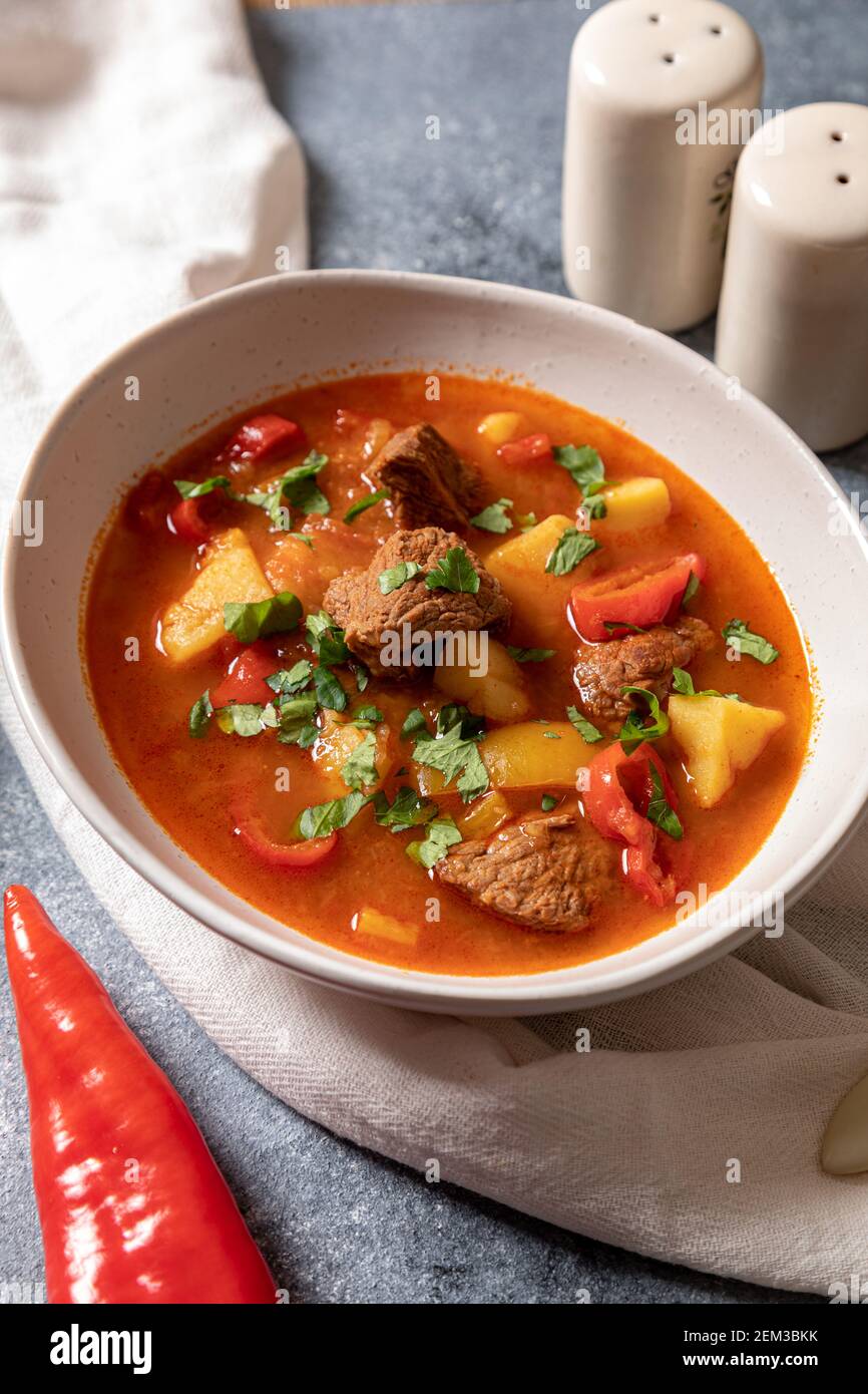 Il goulash è un piatto tradizionale ungherese con manzo, patate, pomodori e peperoni. Goulash in piatti bianchi con verdure per cucinare. Foto Stock