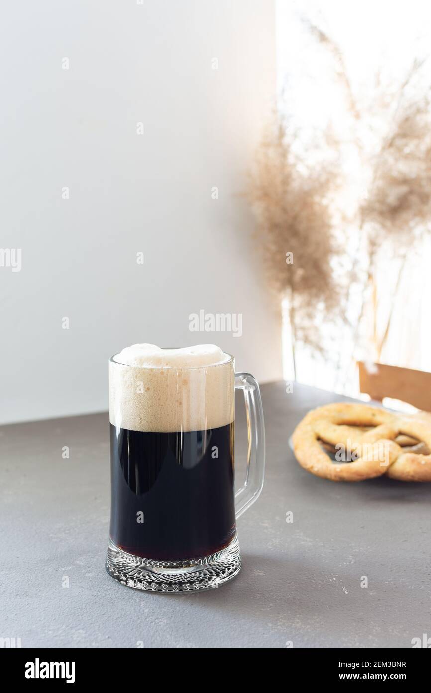 Birra artigianale scura in grande tazza di birra e deliziosa fatta in casa pretzel su sfondo grigio Foto Stock