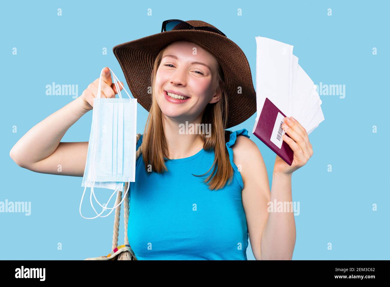 Viaggiare durante una pandemia. Ritratto di una donna turistica in un cappello, con documenti e maschere mediche su sfondo blu. Foto Stock