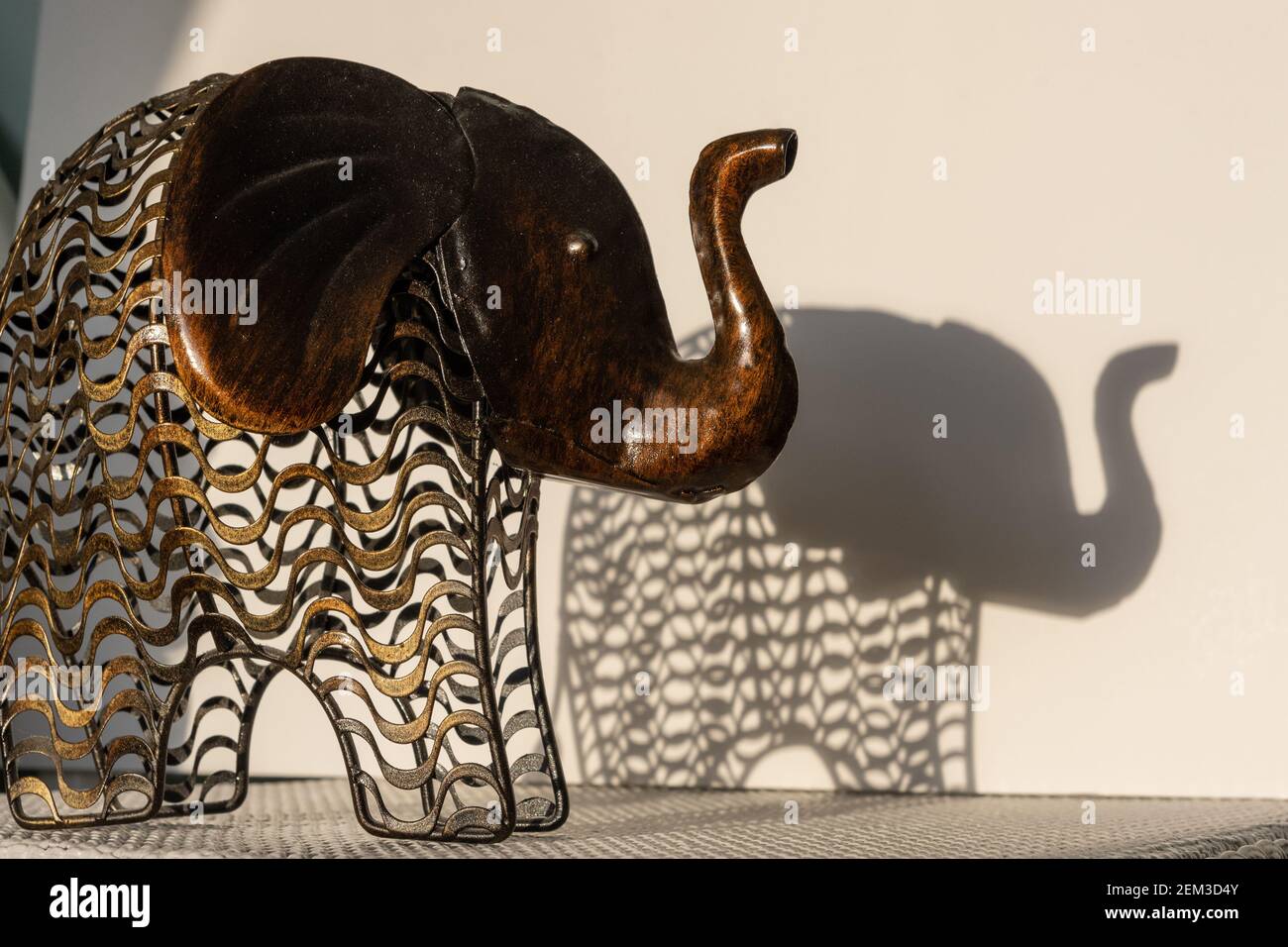 Ornamento di elefante metallico su un tavolo in luce solare diretta creando ombre dure sulla parete; concept shot per l'elefante nella stanza. Foto Stock