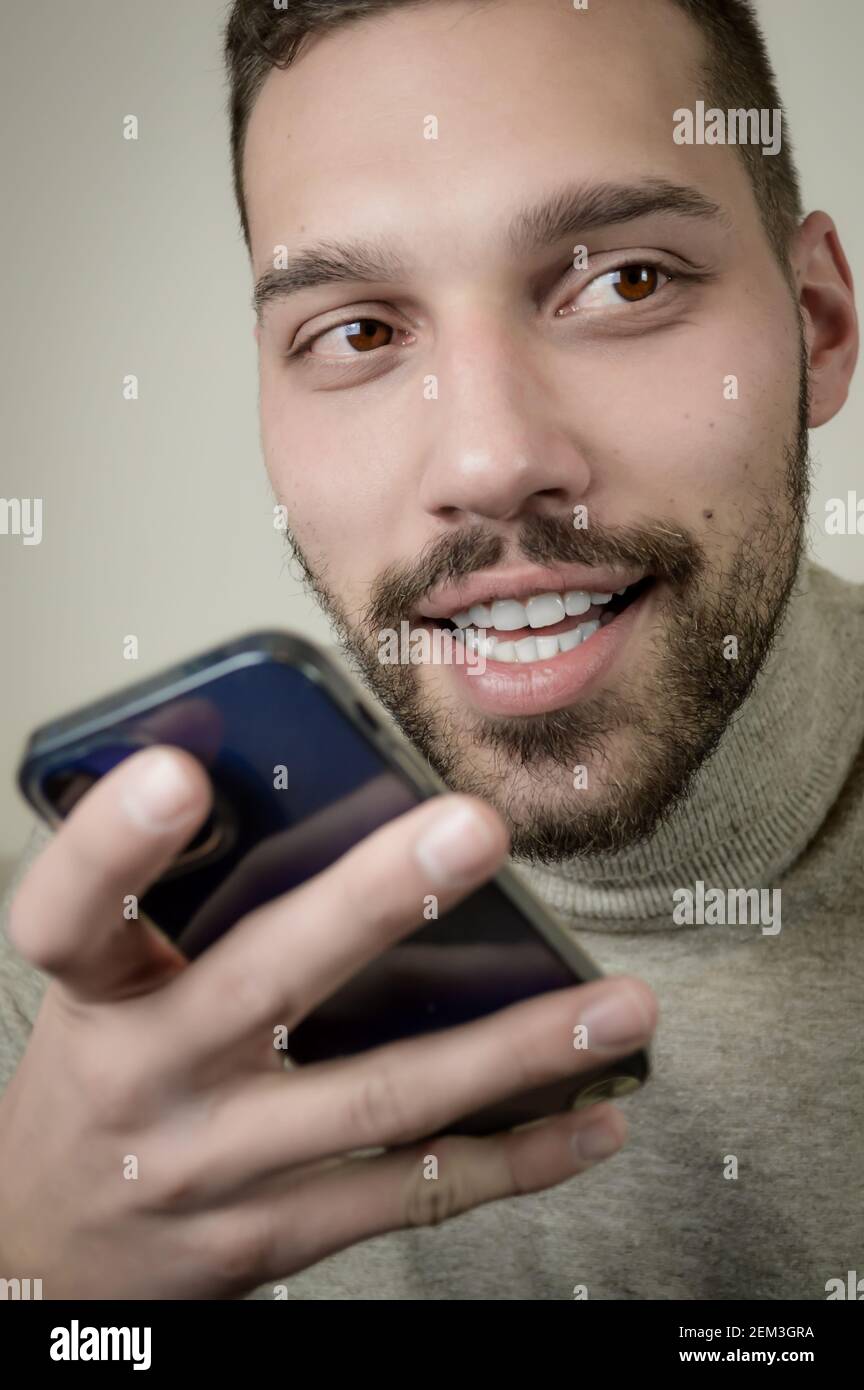Ritratto di un giovane divertito che sta registrando un messaggio audio sullo smartphone Foto Stock