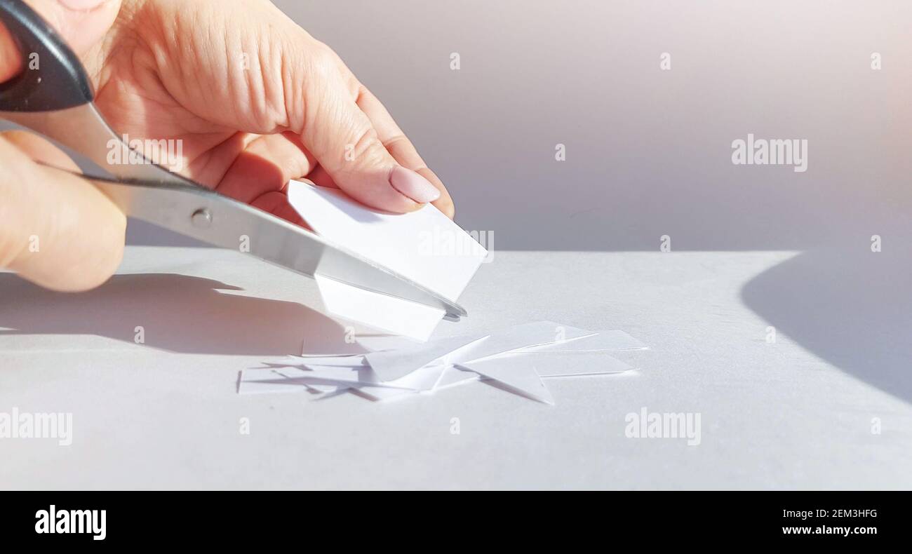 La mano di una donna taglia un foglio di carta bianca con le