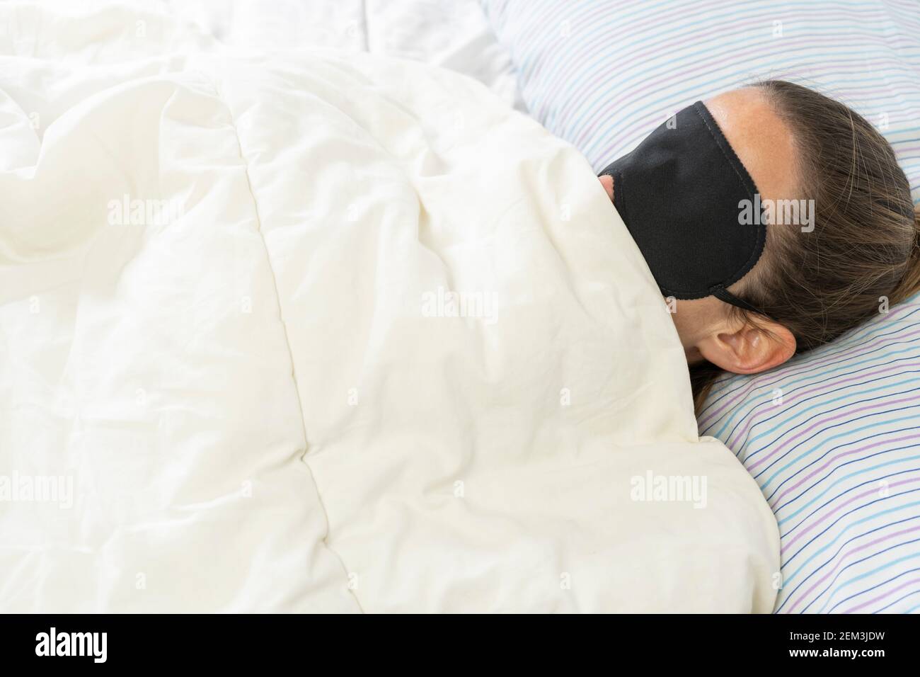 Giovane donna con maschera da sonno coperta di coperta bianca, sdraiata in bed.Insomnia e stile di vita concetto di sonno con spazio di copia per il testo. Foto Stock