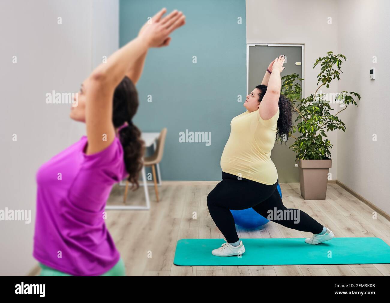 Un'allenatrice femminile conduce allenamenti e stretching per una donna di grandi dimensioni in palestra. allenamento sportivo per la perdita di peso Foto Stock