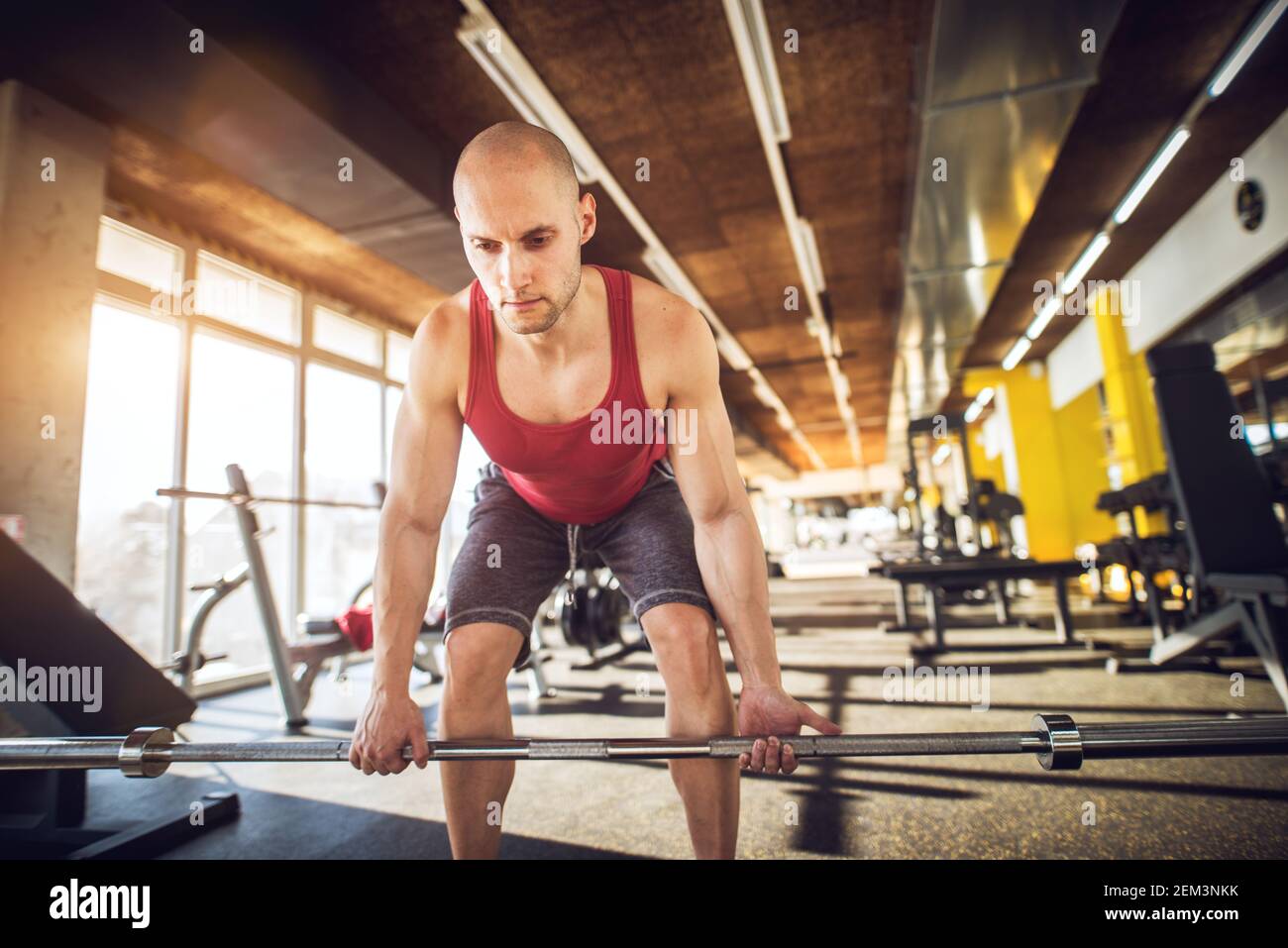 Giovane uomo di fitness sportivo e di lavoro duro messo a fuoco accovacciato con barbell senza pesi e facendo deadlifts in palestra. Foto Stock