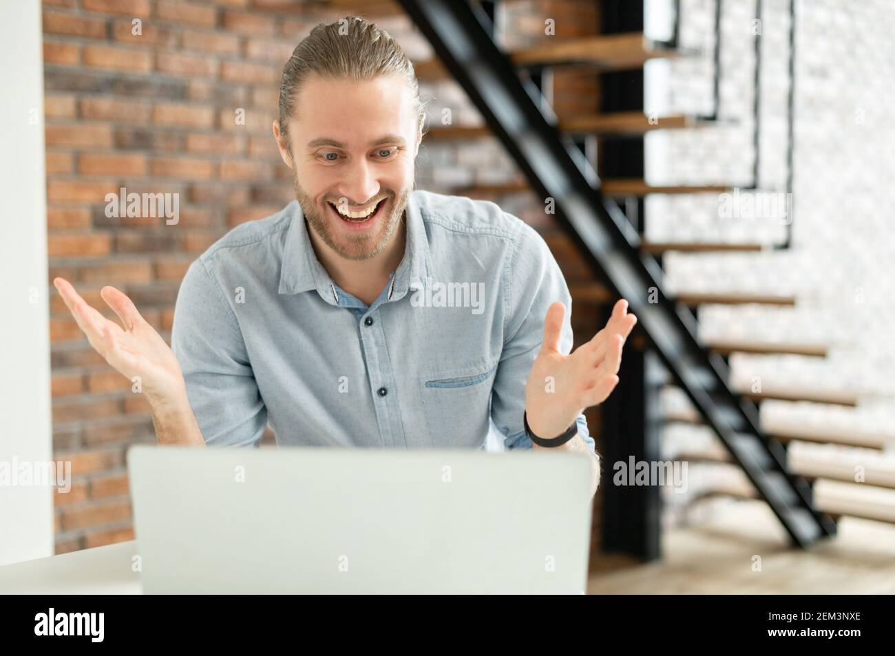 Uomo bello con capelli castani chiari tirati, occhi luminosi e ampio sorriso, non può credere nella sua fortuna, mano sollevata a causa dello stupore, seduto Foto Stock