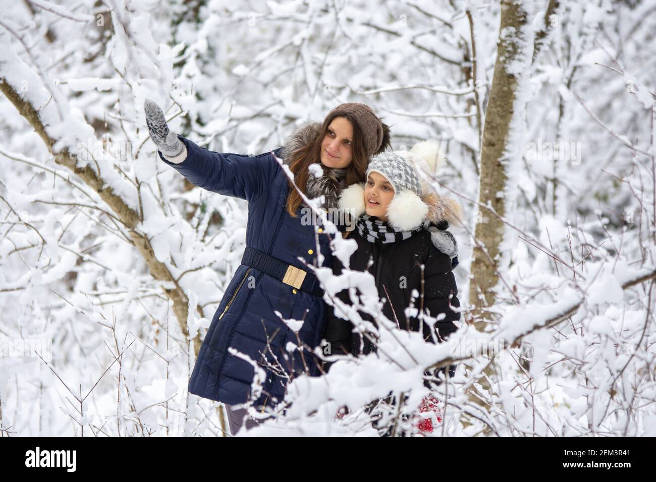 Una ragazza e sua figlia camminano attraverso la foresta innevata, la ragazza mostra qualcosa di interessante Foto Stock