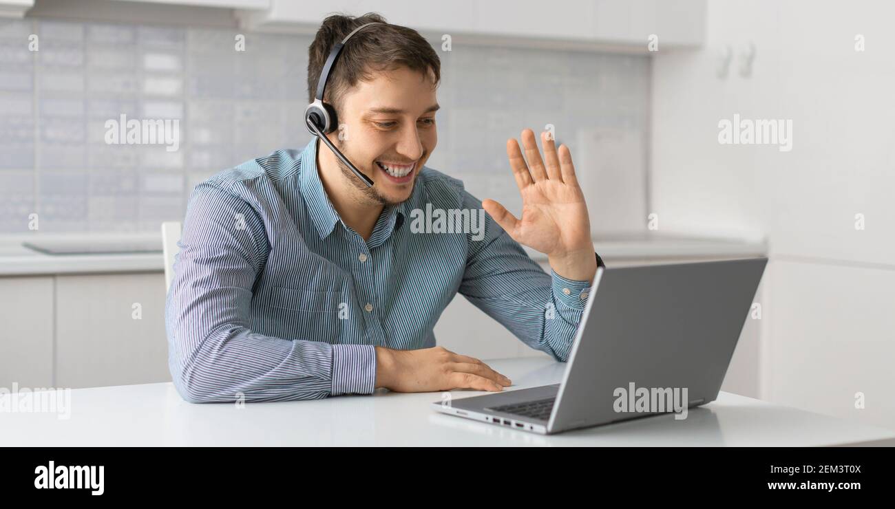 Un uomo che effettua una videochiamata online da casa. Agita la mano e parla di un collegamento video davanti a un monitor laptop. Concetto di tecnologie moderne per Foto Stock