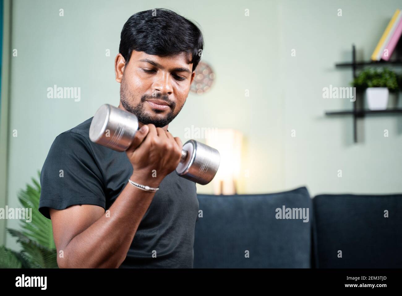 Giovane uomo in allenamento o facendo esercizio con dumbbell a casa - concetto di palestra a casa a causa del coronavirus covid-19 blocco. Foto Stock