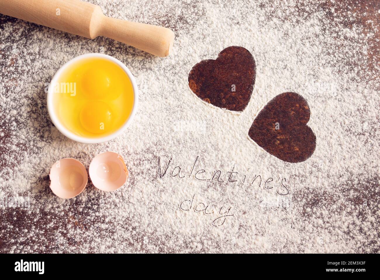 Cospargere la farina con due cuori dipinti su sfondo ligneo, con un tondino e uova. Ricette di cottura. Concetto di San Valentino. Dichiarazione di Foto Stock