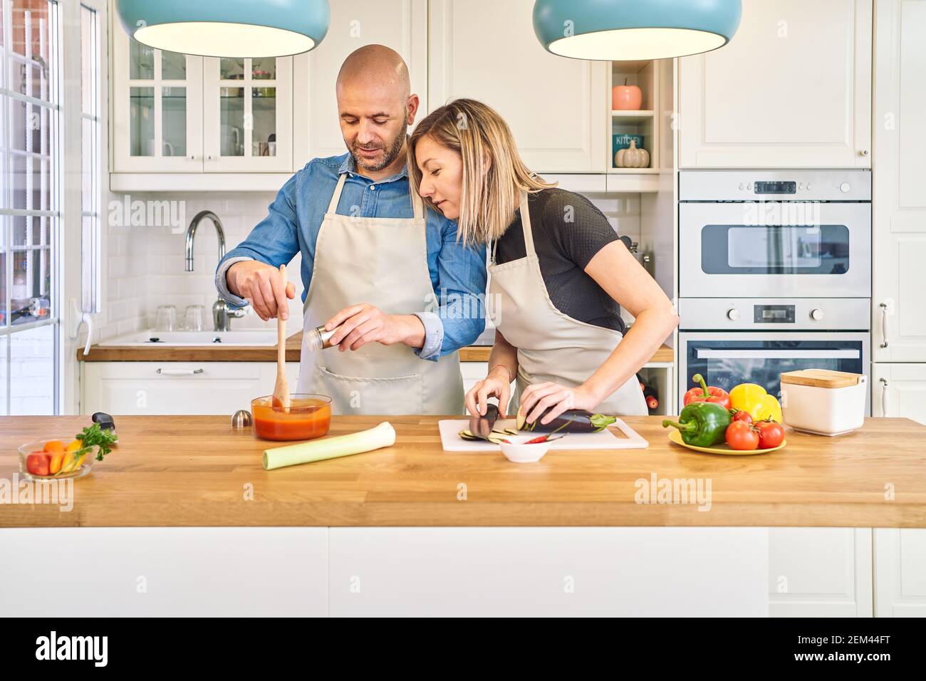 Una giovane coppia felice sta gustando e preparando un pasto sano nella loro cucina. Prepara la salsa di pomodoro mentre lo guarda. Concetto di cibo sano Foto Stock