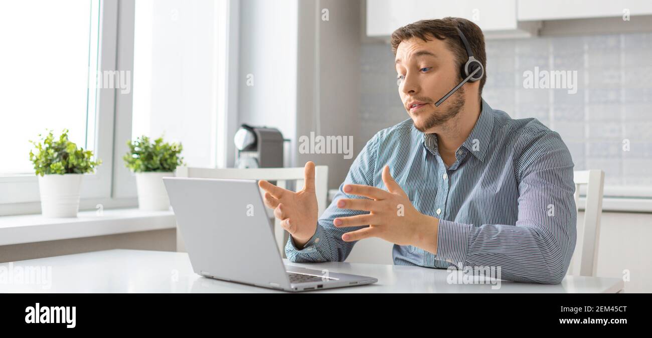 Uomo davanti al computer portatile con cuffia durante una videochiamata online. Concetto di tecnologie moderne per la comunicazione a distanza. Formato 16:9. Foto Stock