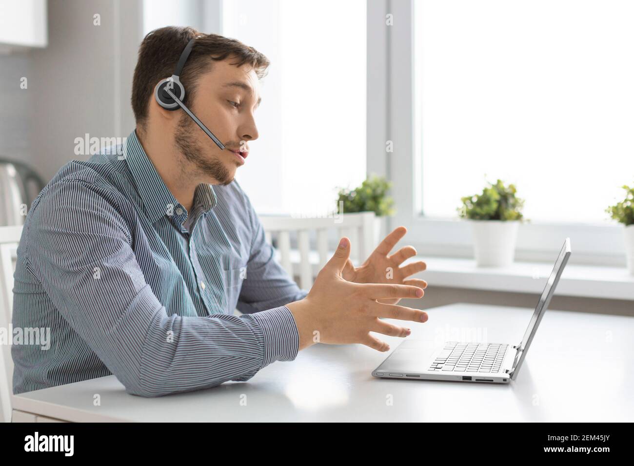 Uomo davanti al computer portatile con cuffia durante una videochiamata online. Concetto di tecnologie moderne per la comunicazione a distanza. Foto Stock