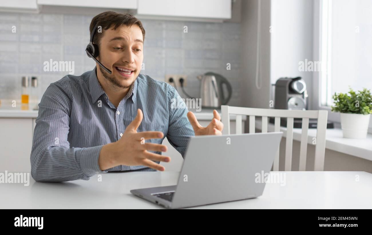 Giovane uomo davanti al computer portatile con cuffia durante una videochiamata online. Concetto di tecnologie moderne per la comunicazione a distanza. Foto Stock