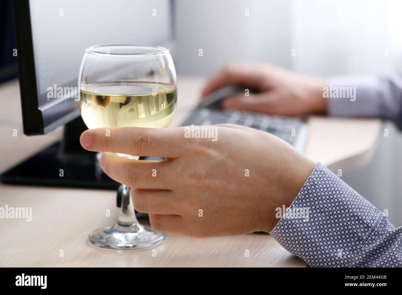 Bicchiere di vino bianco in mano maschile, uomo che beve alcol seduto alla tastiera del PC. Lavoro a distanza a casa o relax in ufficio Foto Stock