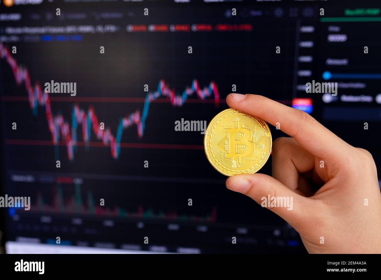 Mano che tiene il bitcoin davanti al grafico con il tasso di cambio. Moneta d'oro criptovaluta Bitcoin. Negoziazione dello scambio di criptovaluta. Bitcoin Foto Stock