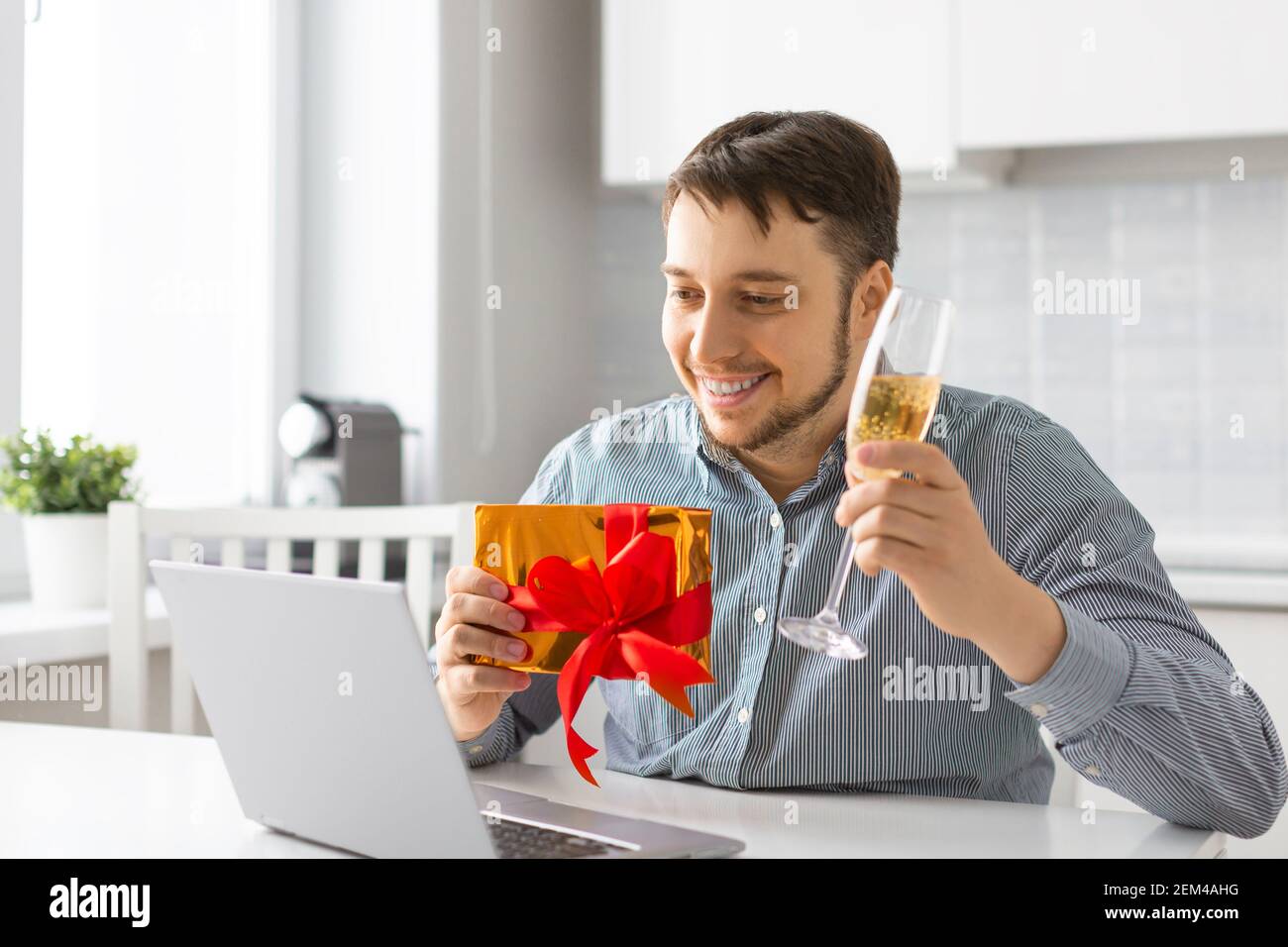 Un uomo con un bicchiere di vino e un giftbox davanti al computer portatile durante una data online. Il concetto di una relazione durante la quarantena. Foto Stock