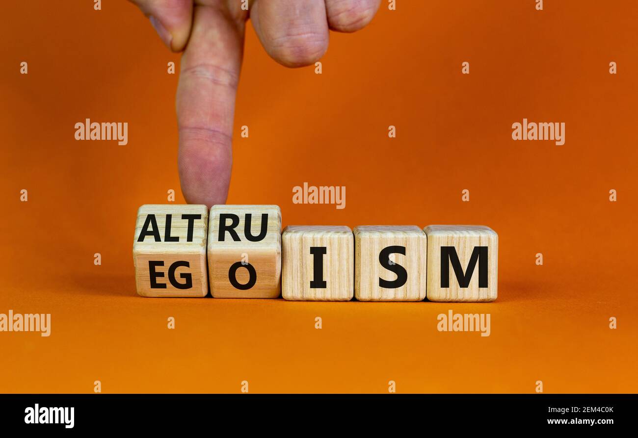 Altruismo o simbolo di egoismo. L'uomo d'affari trasforma i cubetti di legno e cambia la parola 'egoismo' in 'altruismo'. Splendido sfondo arancione, spazio per la copia. Busine Foto Stock