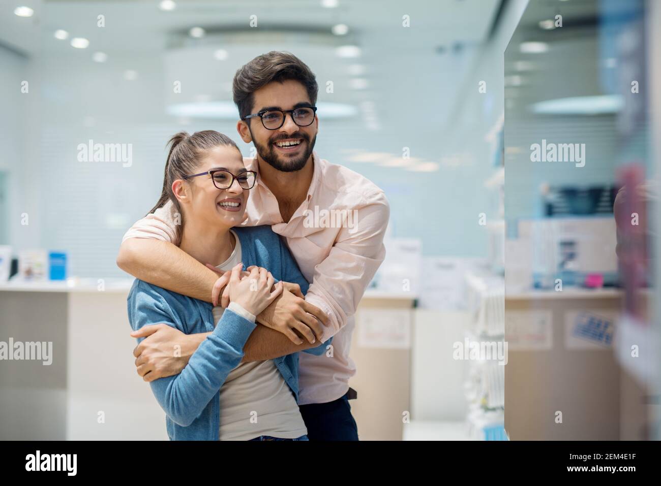 Primo piano ritratto di simpatica ed eccitata giovane coppia di studenti in amore hugging e guardando il grande nuovo tv in un negozio di tecnologia. Foto Stock