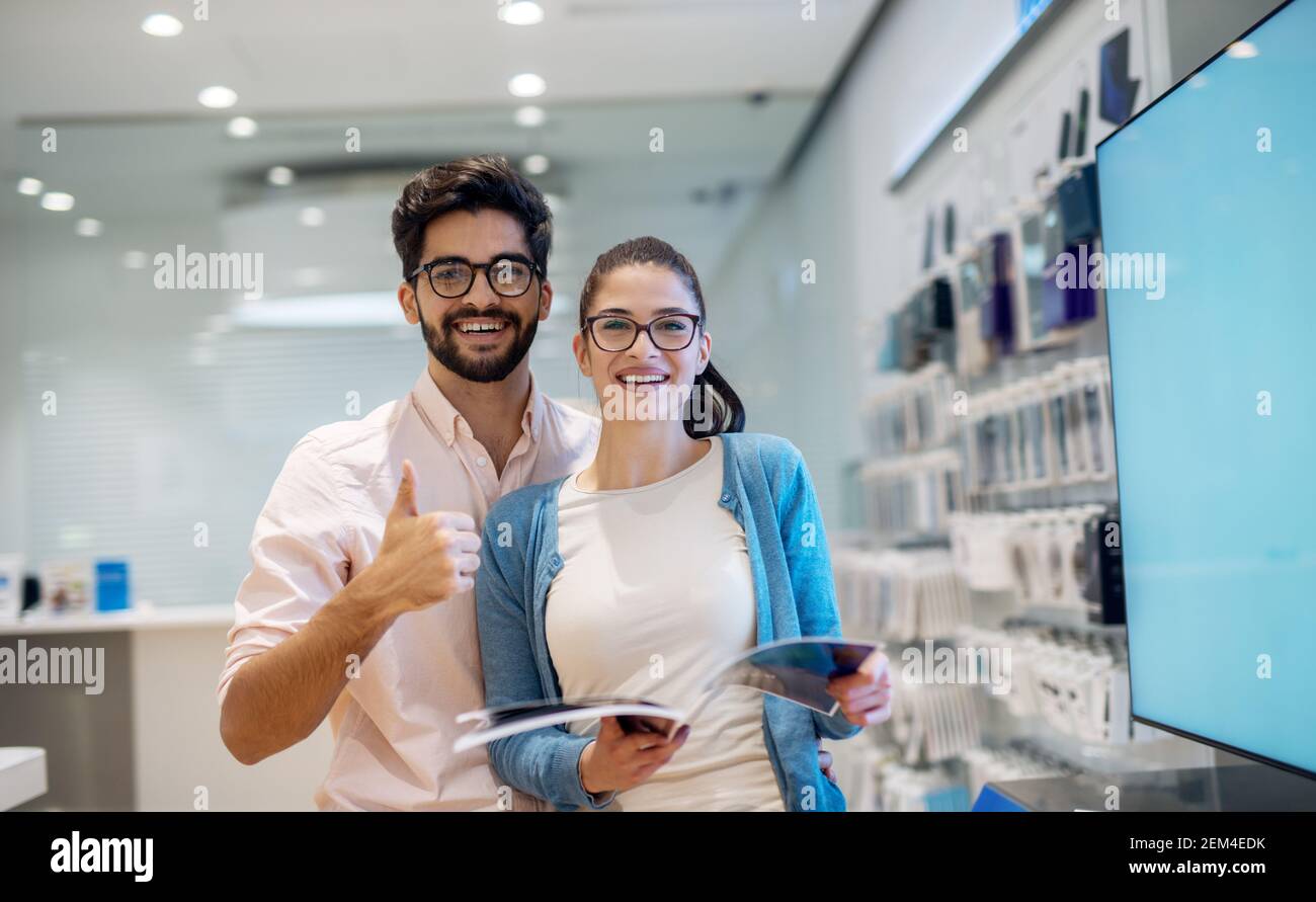 Ritratto di bella emozionata sorridente giovane studentessa con gli occhiali che leggono la specifica mentre il suo ragazzo sta vicino a. lei e. Foto Stock