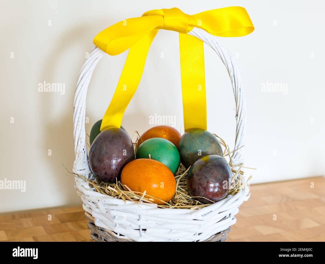 Ancora vita di uova di Pasqua colorate in marmo in cestino di salice con nastro giallo Foto Stock