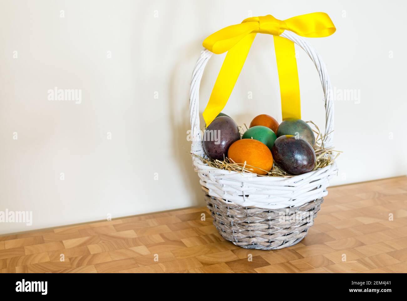 Ancora vita di uova di Pasqua colorate in marmo in cestino di salice con nastro giallo Foto Stock
