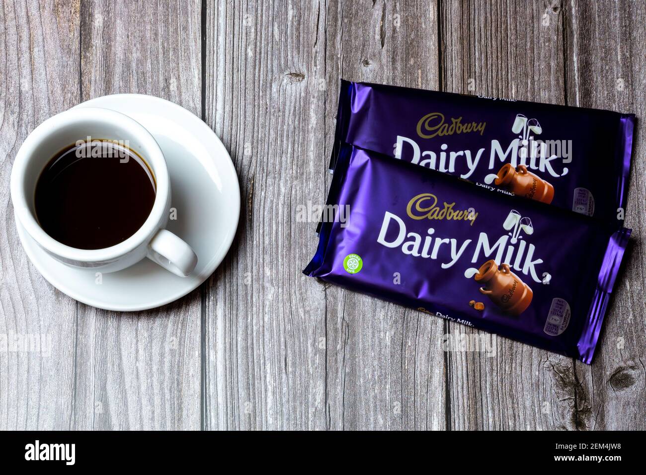 Due bar di cioccolato al latte Cadbury Dairy su un tavolo di legno accanto ad una tazza di caffè Foto Stock