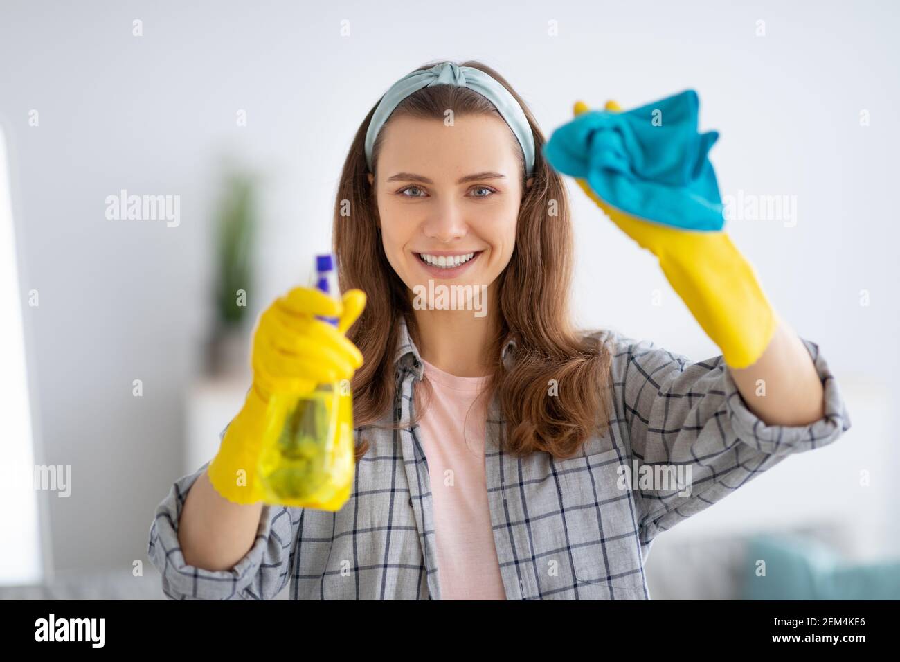 Ritratto di giovane donna sorridente in guanti di gomma per la pulizia del vetro con detergente spray, all'interno Foto Stock