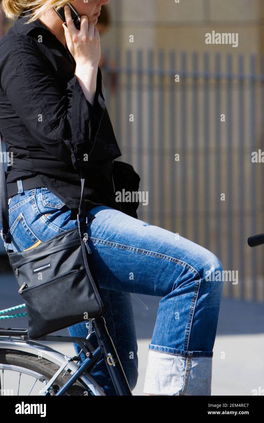 Profilo laterale di una giovane donna seduta su una bicicletta e utilizzando un telefono cellulare Foto Stock