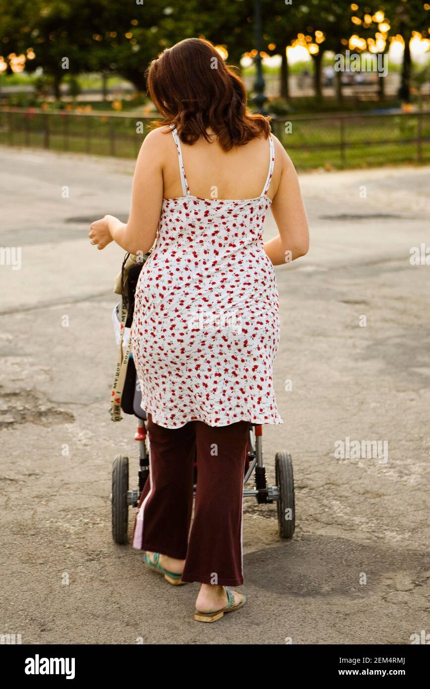Vista posteriore di una giovane donna che spinge un passeggino in viaggio Foto Stock