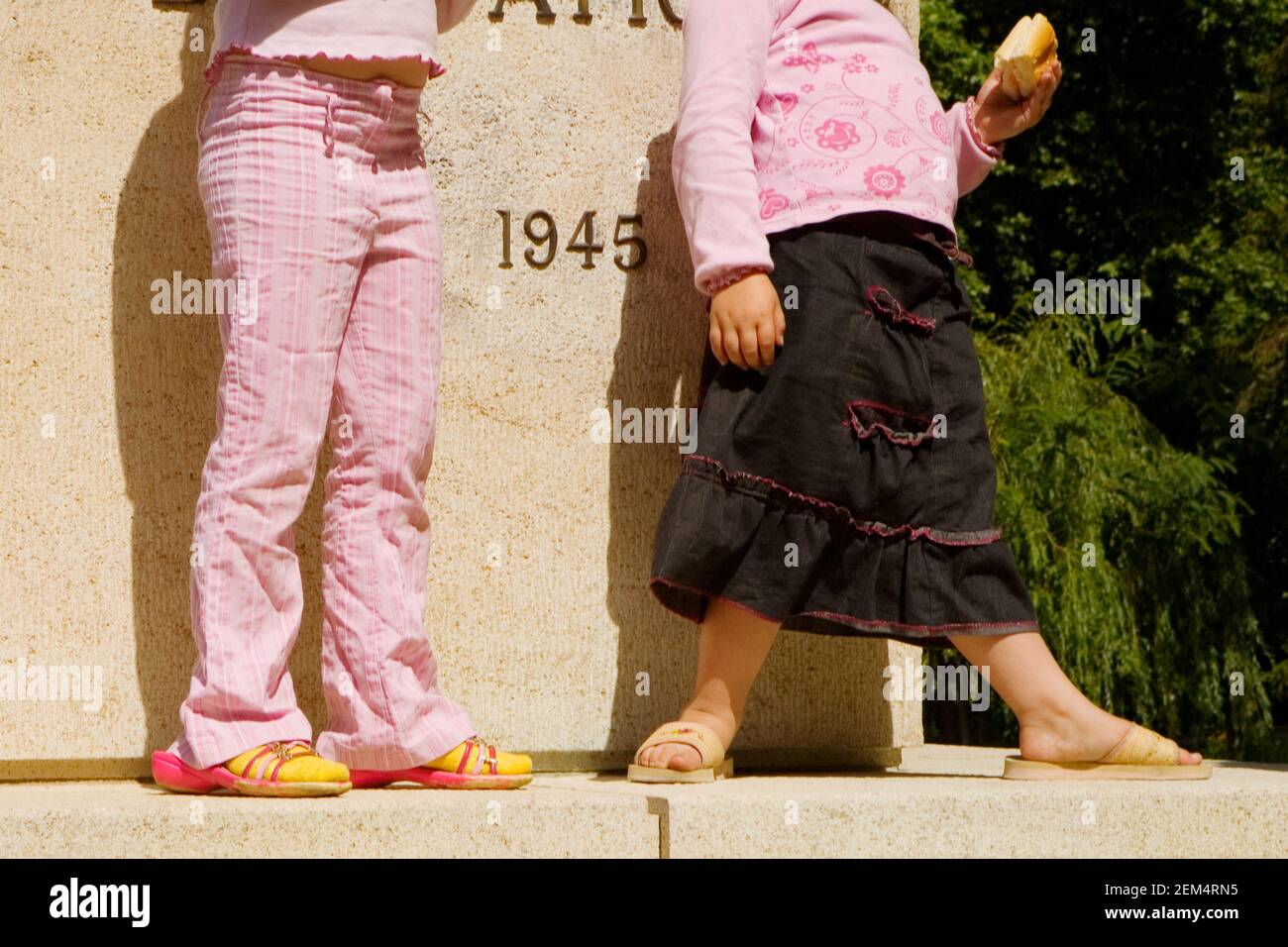 Vista in sezione bassa di due ragazze in piedi di fronte un memoriale di guerra Foto Stock