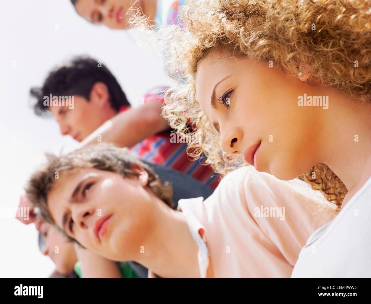 Vista ad angolo basso di una ragazza adolescente e di una giovane uomo con i loro amici sullo sfondo Foto Stock