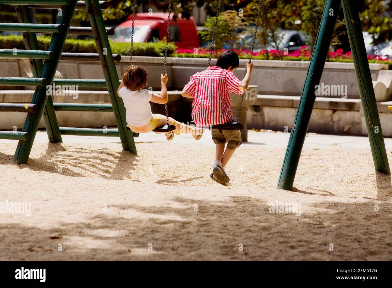 Vista posteriore di un ragazzo e di una ragazza che oscillano su un'altalena, Madrid, Spagna Foto Stock