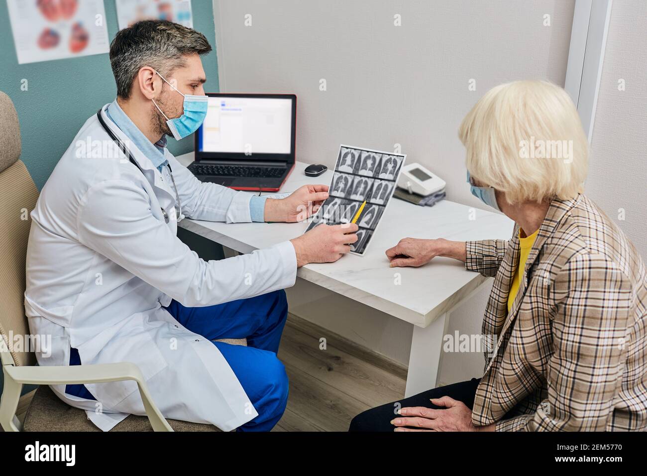 Medico maschile che analizza per il paziente anziano una scansione TC dei polmoni. Polmonite, coronavirus, malattie polmonari Foto Stock