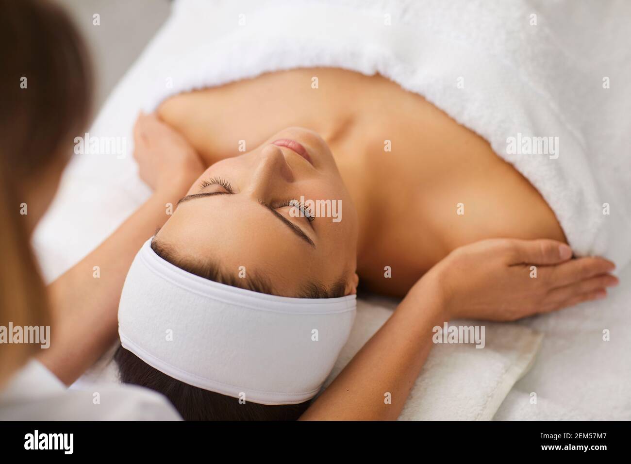 Cosmetologo o massaggiatore che effettua un massaggio manuale rilassante ringiovanente per il viso e spalle per donna Foto Stock
