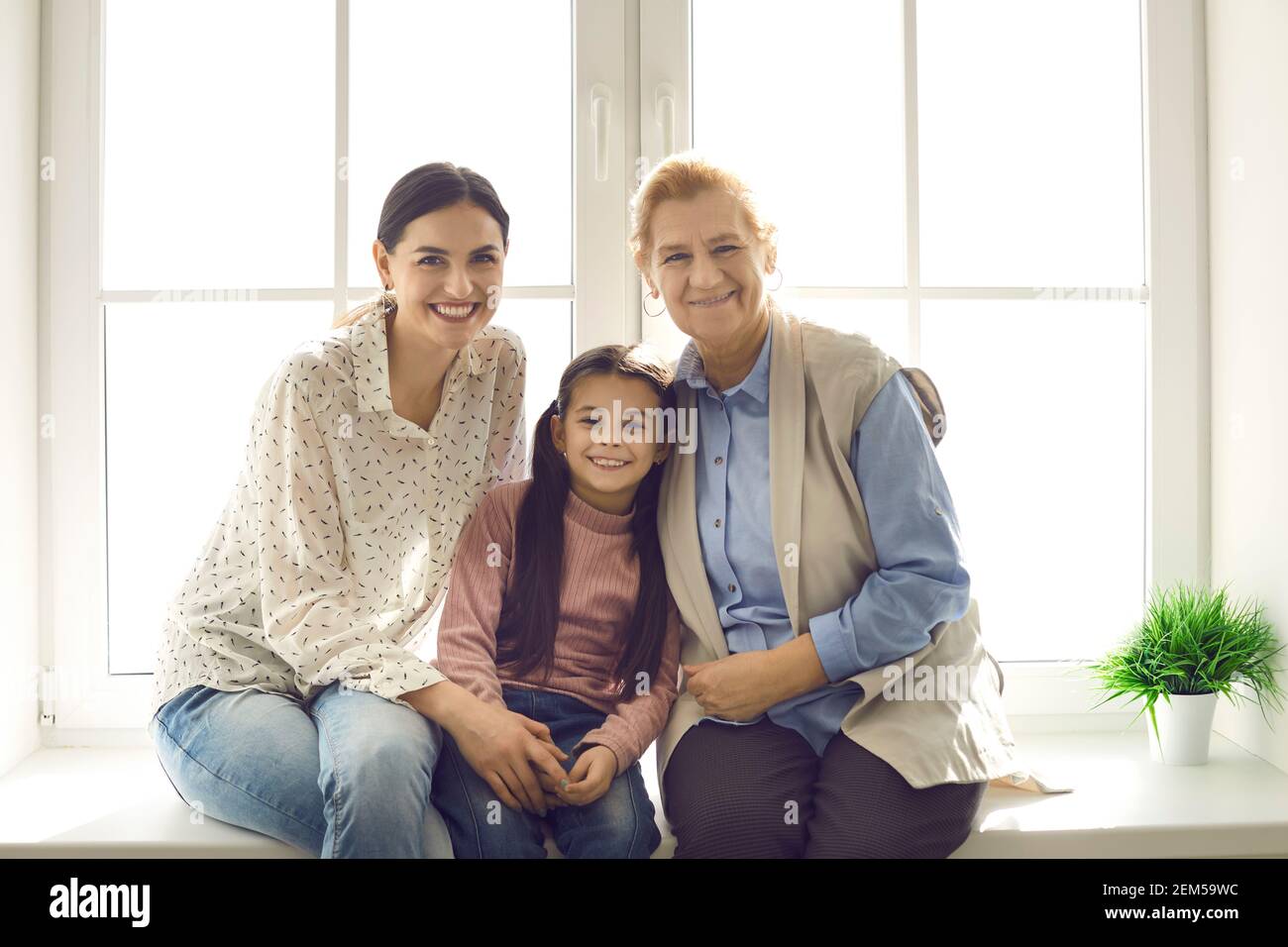 Ritratto di madre felice, figlia e nonna seduta insieme sul davanzale Foto Stock