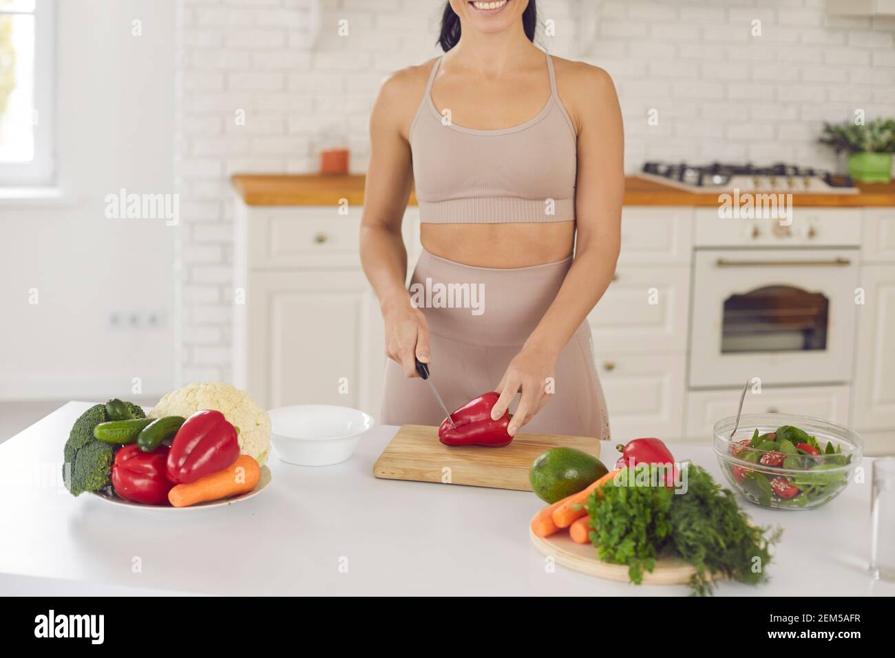 Un taglio corto di donna felice tritare i peperoni mentre si fa sano insalata vegetariana Foto Stock