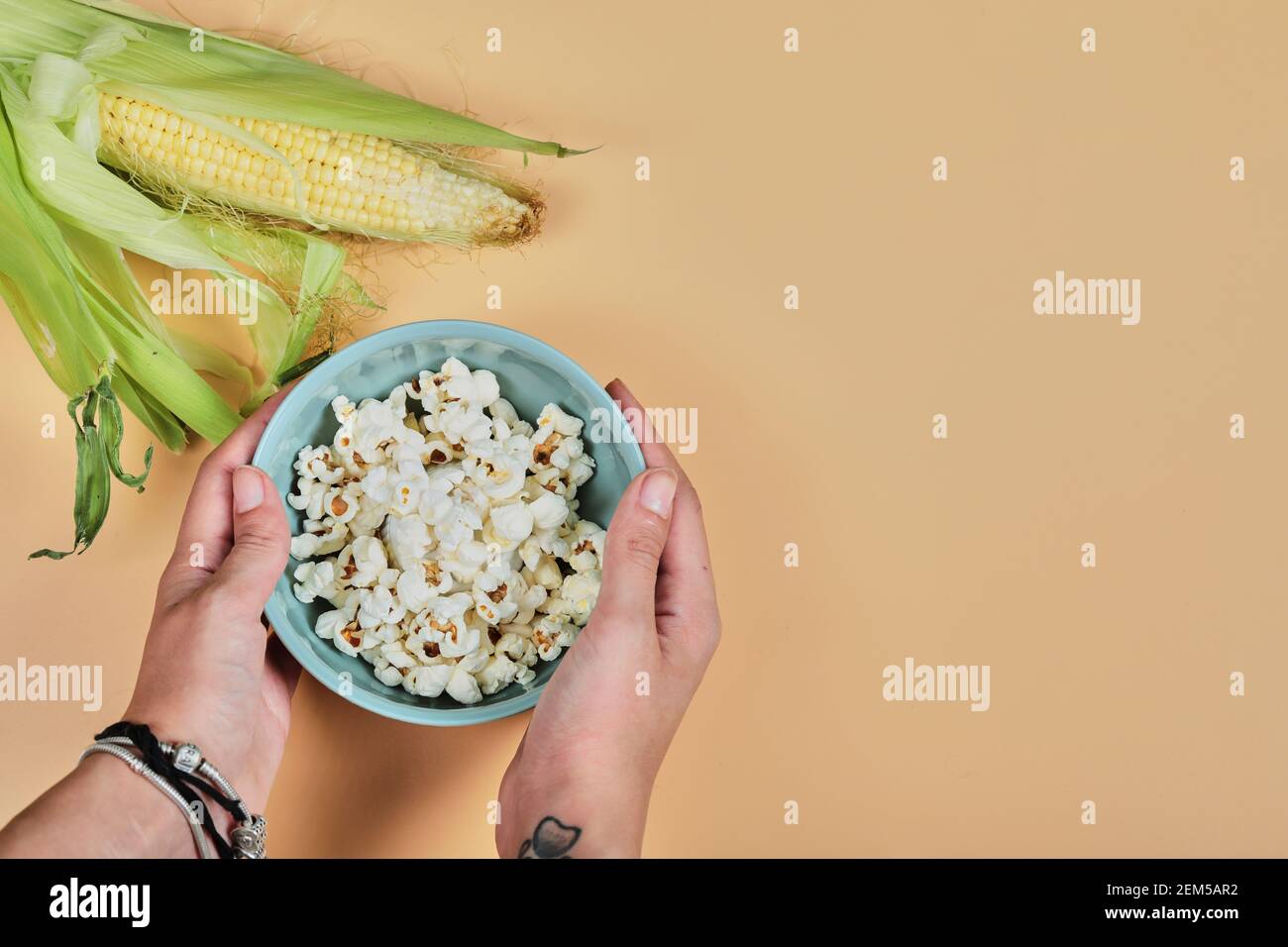 Tenere a mano la ciotola di popcorn e mais su sfondo arancione Foto Stock