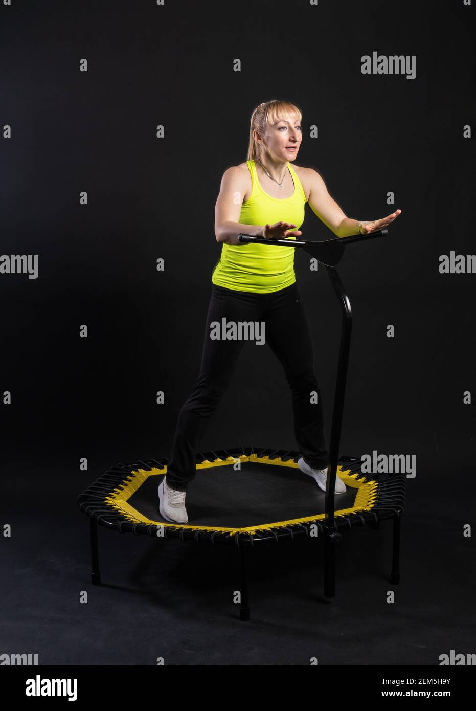 Ragazza su un trampolino fitness su sfondo nero in una t-shirt gialla donna, movimento del corpo attrezzatura, rimbalzo muscolare. Movimento bianco del mosca, mus fisico Foto Stock